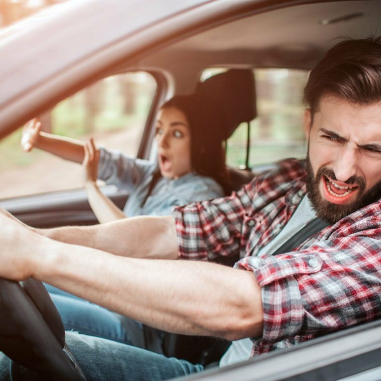 Bearded man is driving car. They are riding too fast. Guy is keeping his eyes closed but still driving car. Girl is keeping her hands in front of her. She is trying to defence herself